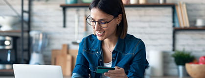 A woman holding credit card for online payment with computer at home