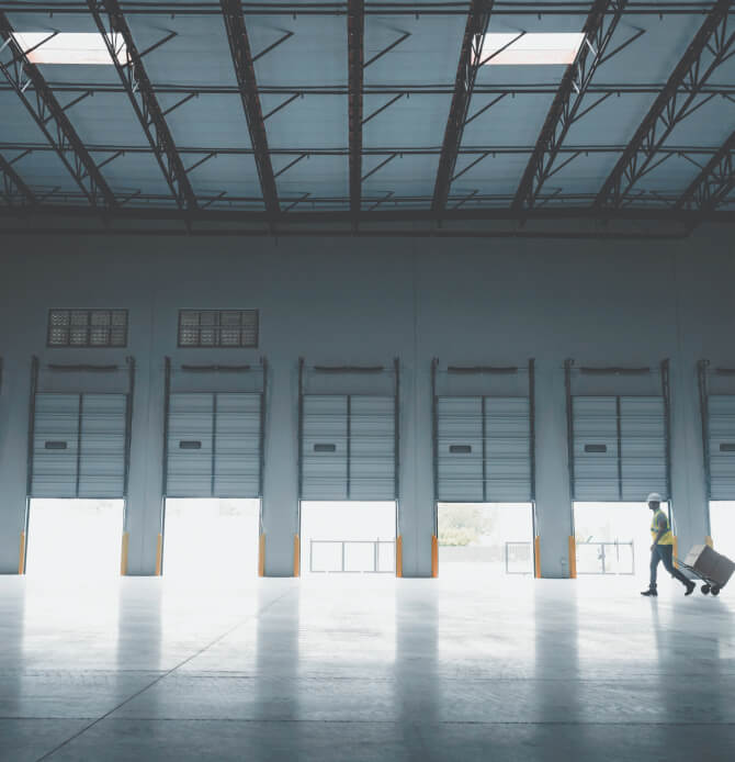 A man in a hard hat and reflective vest walking past six open loading doors