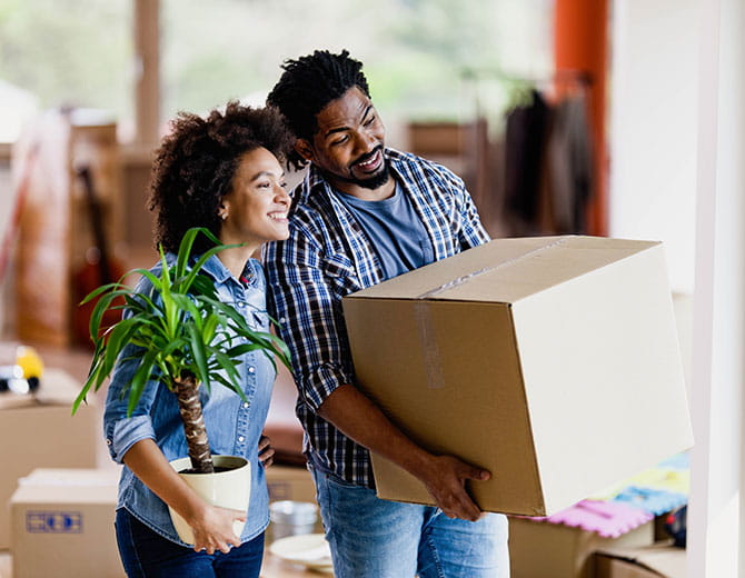 Smiling man carries box, smiling woman carries plant.
